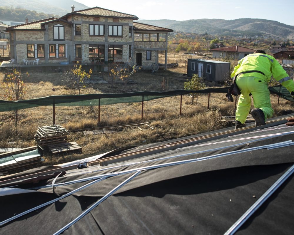 Worker on the top of the house making roof. Building a new house with black roof. Repair and build construction of roof. Conception for roofing, new home, real estate and constructions.