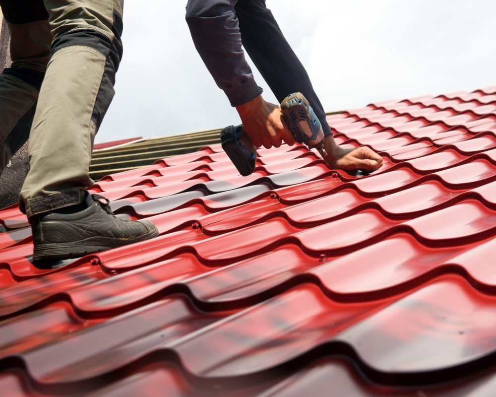 Roofer working on roof structure of building on construction site,Roofer using air or pneumatic nail gun and installing Metal Sheet on top new roof.